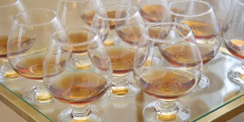 Viele Gläser mit bernsteinfarbenem Metaxa stehen bereit. Was ist Metaxa? Ein griechischer Weinbrand, der nach einer geheimen Rezeptur hergestellt wird.