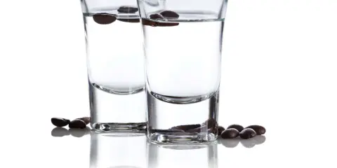 Zwei Gläser mit klarem Schnaps, darin schwimmende Kaffeebohnen. Der Sambuca-Prozent ist hier gut sichtbar.
