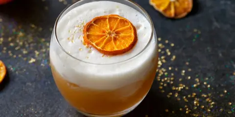 Ein cremiger Amaretto Cocktail mit einem getrockneten Orangenscheibchen und goldenem Glitzer.