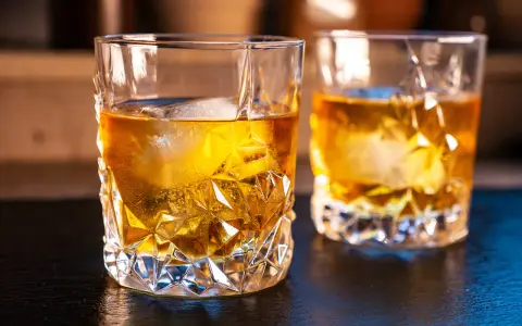 Zwei Gläser mit bernsteinfarbenem on the rocks drink, Eiswürfel schmelzen langsam.