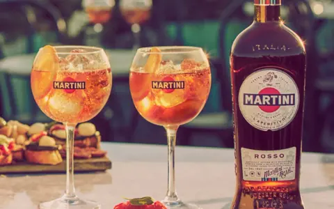 Zwei Gläser Martini mit Eis und Orangenscheibe, daneben eine Flasche Martini Rosso. Perfekt für den Aperitif, mit dem richtigen Martini prozent.