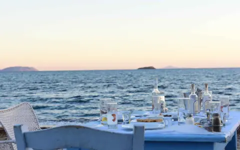 Tisch am Meer mit Ouzo-Flaschen, Gläsern und Essen. Der Ouzo-Prozent ist perfekt für den Sonnenuntergang.