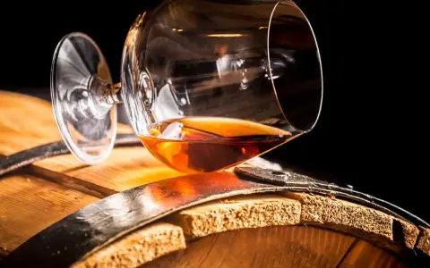 Ein Glas bernsteinfarbener Brandy ruht auf einem Holzfass. So sieht aus, was ein Brandy ist: ein edler Tropfen.