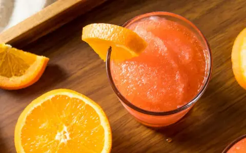 Gefrorene Aperol Spritz Varianten mit frischen Orangenscheiben auf Holztisch.