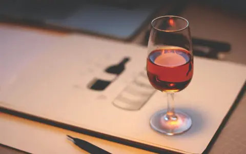 Ein Glas Portwein steht auf einem Skizzenbuch, das eine Flasche zeigt. Perfekt, um zu lernen, wie trinkt man Portwein.