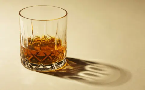 Ein Glas Whisky mit starkem Schatten auf hellem Hintergrund.