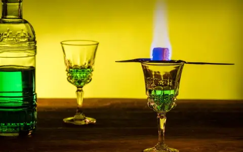 Grüner Absinth brennt in einem Glas, ein Zuckerwürfel karamellisiert. Die Zubereitung erinnert an die traditionelle Absinth Herkunft.