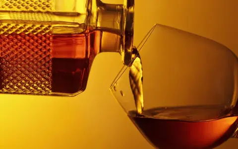 Bernsteinfarbener Armagnac fließt aus einer Karaffe in ein Glas. Was ist das? Ein edler Weinbrand aus Frankreich.