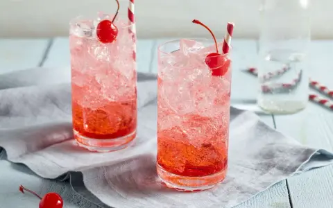 Zwei erfrischende Getränke mit Eis, Kirschen und Strohhalmen. Die rote Farbe verrät, was ist Grenadine: ein süßer Sirup aus Granatäpfeln.
