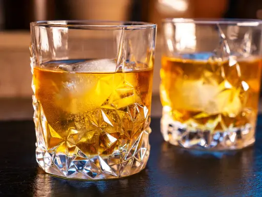 Zwei Gläser mit bernsteinfarbenem on the rocks drink, Eiswürfel schmelzen langsam.