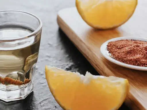 Ein Glas Tequila mit Wurm, daneben Orangenstücke und eine Schale mit Gewürzmischung.