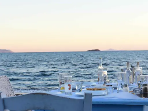 Tisch am Meer mit Ouzo-Flaschen, Gläsern und Essen. Der Ouzo-Prozent ist perfekt für den Sonnenuntergang.