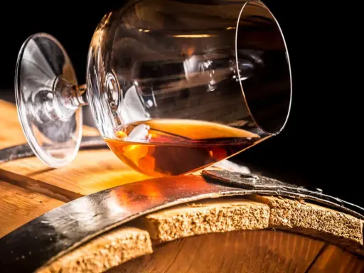 Ein Glas bernsteinfarbener Brandy ruht auf einem Holzfass. So sieht aus, was ein Brandy ist: ein edler Tropfen.