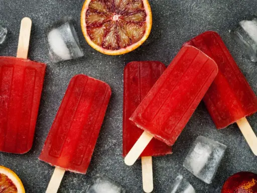 Erfrischende Eis am Stiel mit Campari Orange Geschmack, umgeben von Eiswürfeln und Blutorangen-Scheiben.