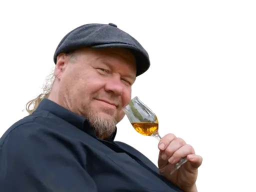 Ein Mann mit Schiebermütze und Bart hält ein Glas bernsteinfarbenen Rum. Er scheint zu wissen, wie man Rum genießt.