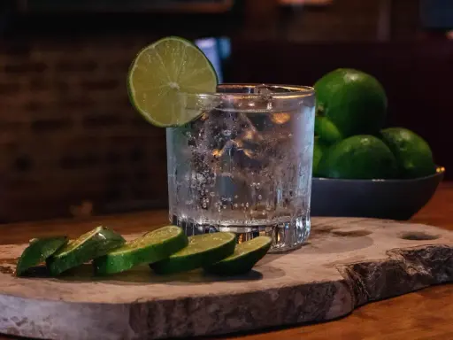 Erfrischendes Glas mit Eis, Limettenscheiben und einer Schale voller Limetten – perfekt für ein Tonic Water Rezept.