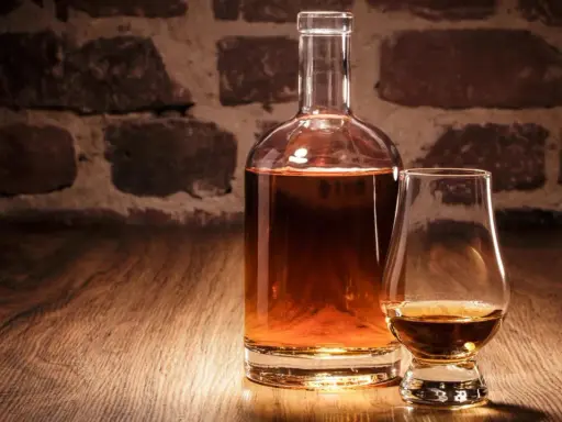 Eine Karaffe und ein Glas mit bernsteinfarbenem Whisky vor einer Ziegelwand. Verschiedene Whisky-Sorten laden zum Genuss ein.