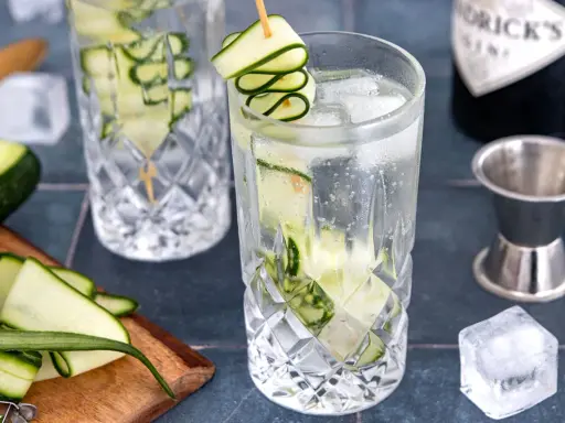 Erfrischendes Gin Tonic Rezept mit Gurke: Eisgekühlte Gläser, frische Gurkenscheiben und eine Flasche Gin.