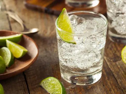 Erfrischender Gin pur trinken mit Eis und Limettenspalten. Frische Limetten liegen daneben.