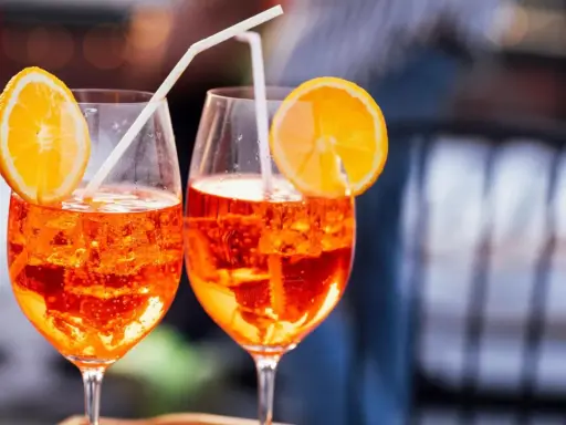 Zwei Aperol Spritz mit Orangenscheiben und Strohhalmen. Der leuchtende Aperol Farbstoff schimmert in den Gläsern.