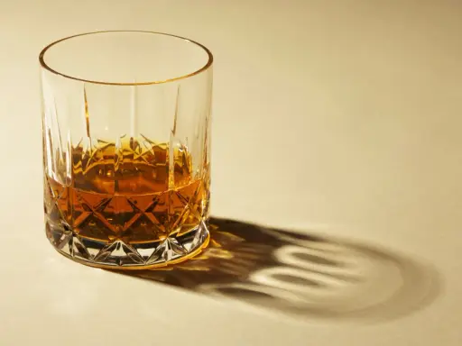 Ein Glas Whisky mit starkem Schatten auf hellem Hintergrund.