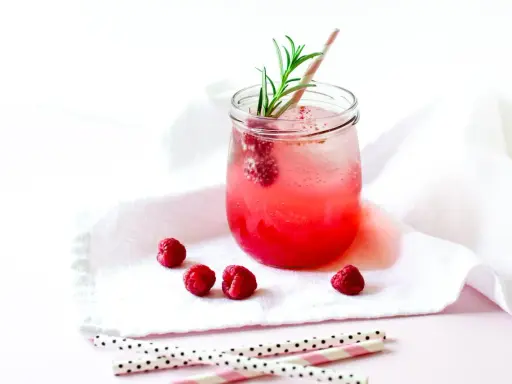 Erfrischender Gin Tonic mit Himbeeren, garniert mit Rosmarin. Ein süßer Genuss an einem warmen Tag.