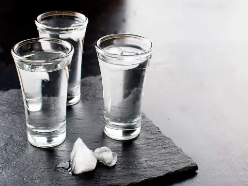Drei Gläser Wodka mit Eiswürfeln auf schwarzem Schiefer. Wodka wird aus Getreide oder Kartoffeln hergestellt.