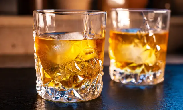 Zwei Gläser mit bernsteinfarbenem on the rocks drink, Eiswürfel schmelzen langsam.