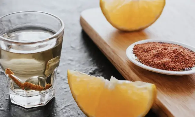 Ein Glas Tequila mit Wurm, daneben Orangenstücke und eine Schale mit Gewürzmischung.
