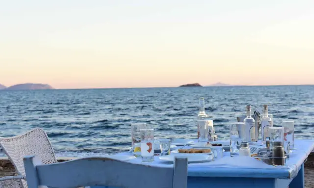 Tisch am Meer mit Ouzo-Flaschen, Gläsern und Essen. Der Ouzo-Prozent ist perfekt für den Sonnenuntergang.