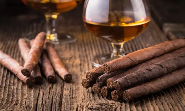 Zwei Gläser Cognac und Zigarren auf Holztisch. So trinkt man Cognac: langsam und genussvoll.