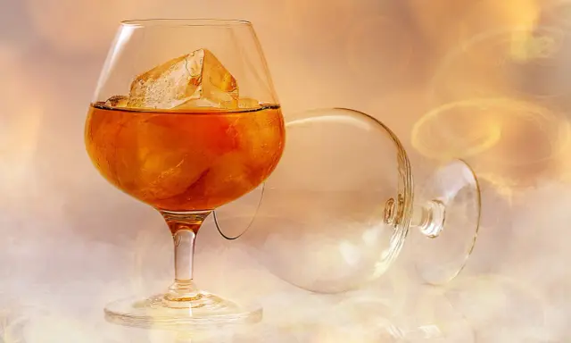 Ein Glas bernsteinfarbener Brandy mit Eiswürfeln, daneben ein leeres, umgekipptes Glas. Man fragt sich, wie schmeckt brandy.