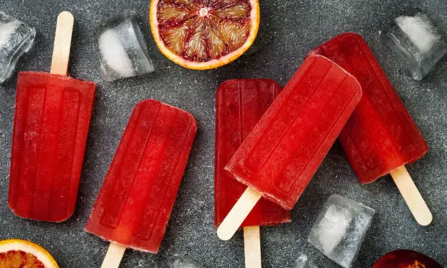 Erfrischende Eis am Stiel mit Campari Orange Geschmack, umgeben von Eiswürfeln und Blutorangen-Scheiben.