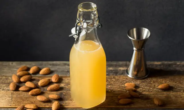 Flasche mit selbstgemachtem Mandelsirup, umgeben von Mandeln und einem Messbecher. Perfekt, um Mandelsirup selber zu machen!