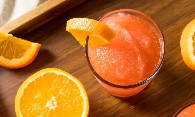 Gefrorene Aperol Spritz Varianten mit frischen Orangenscheiben auf Holztisch.