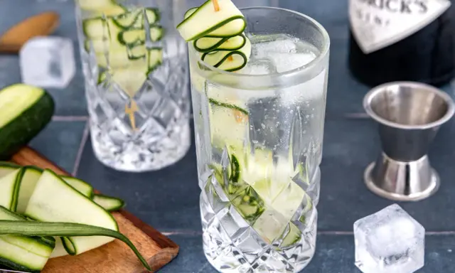 Erfrischendes Gin Tonic Rezept mit Gurke: Eisgekühlte Gläser, frische Gurkenscheiben und eine Flasche Gin.