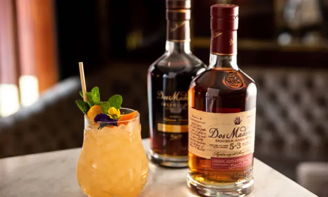 Ein erfrischender Cocktail mit Minze und Früchten neben zwei Flaschen Dos Maderas Rum. Der Alkoholgehalt des Rums ist auf dem Etikett angegeben.
