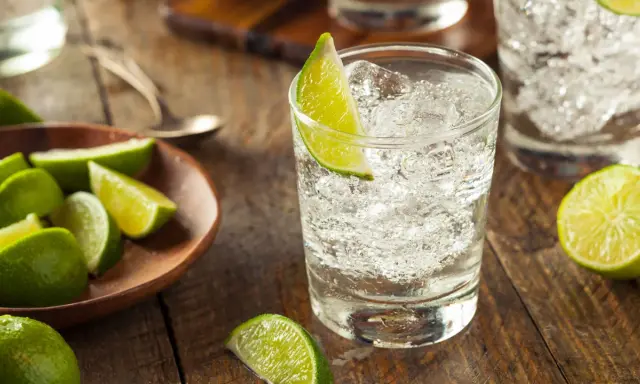 Erfrischender Gin und Bitter Lemon mit Eis und Limettenspalten auf rustikalem Holztisch.
