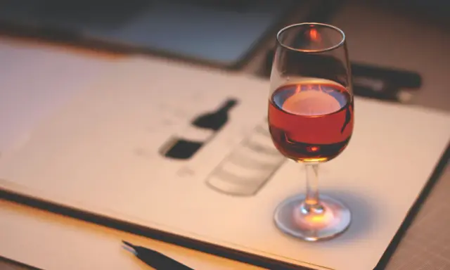 Ein Glas Portwein steht auf einem Skizzenbuch, das eine Flasche zeigt. Perfekt, um zu lernen, wie trinkt man Portwein.