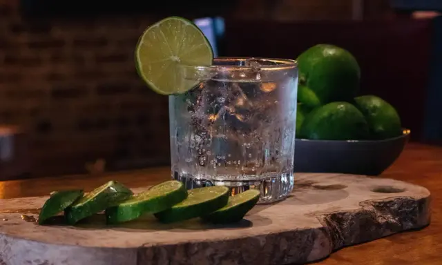 Erfrischender Gin Tonic mit Eis, Limettenscheiben und einer Schale voller Limetten. Perfekt für einen warmen Abend.