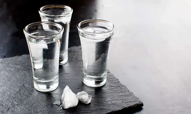 Drei Gläser Wodka mit Eiswürfeln auf schwarzem Schiefer. Wodka wird aus Getreide oder Kartoffeln hergestellt.
