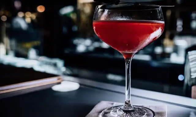 Ein roter Sloe Gin Tonic in einem eleganten Glas, garniert mit einer dunklen Zweigspitze, steht auf einem Tisch.
