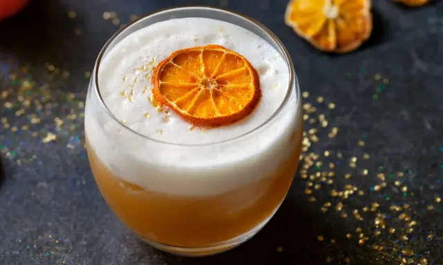 Ein cremiger Amaretto Cocktail mit einem getrockneten Orangenscheibchen und goldenem Glitzer.