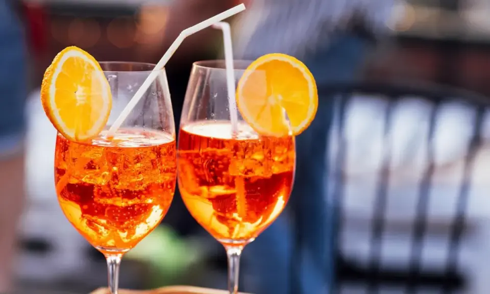 Zwei Aperol Spritz mit Orangenscheiben und Strohhalmen. Der leuchtende Aperol Farbstoff schimmert in den Gläsern.
