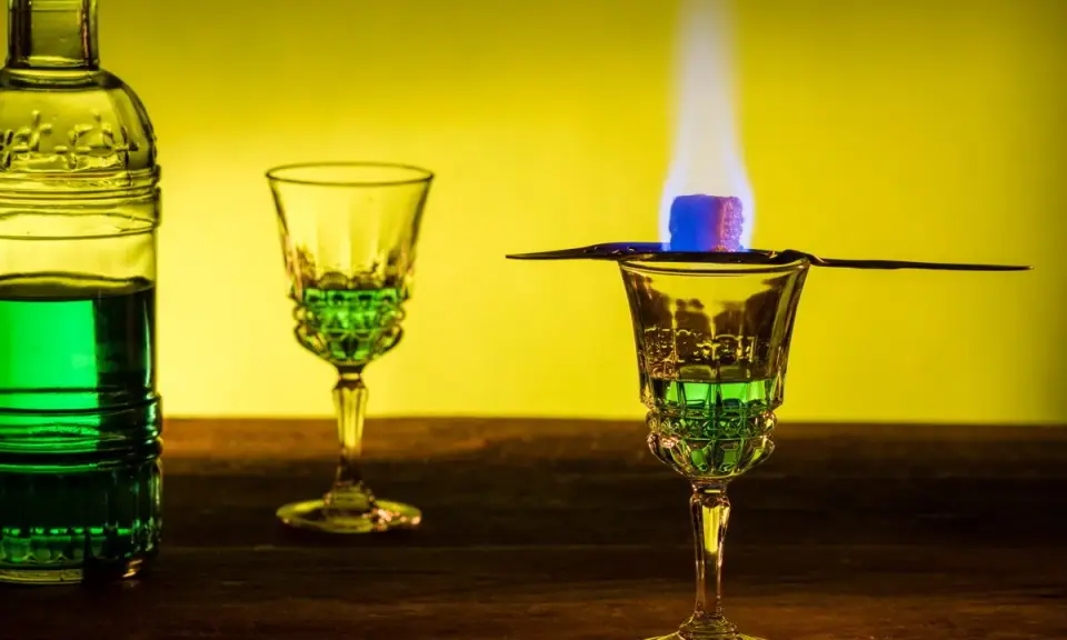 Grüner Absinth brennt in einem Glas, ein Zuckerwürfel karamellisiert. Die Zubereitung erinnert an die traditionelle Absinth Herkunft.