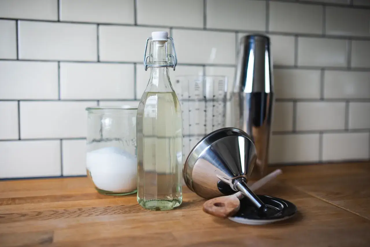 Zutaten für zuckersirup selber machen: Zucker in einem Glas, eine Flasche Sirup, ein Messbecher und ein Cocktailshaker.