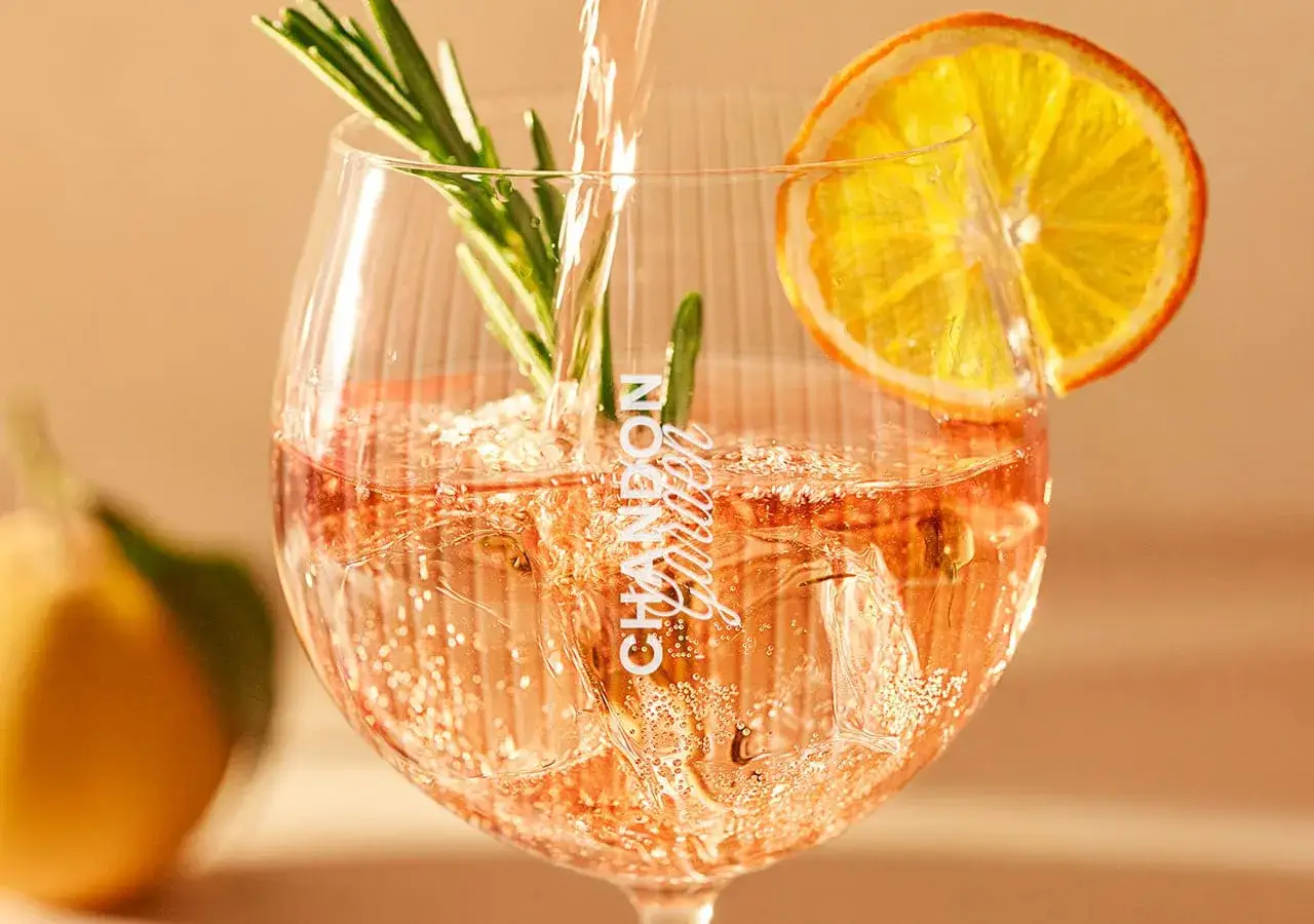 Ein erfrischender Chandon Spritz mit Rosmarin und Orangenscheibe, sprudelnd und eisgekühlt.