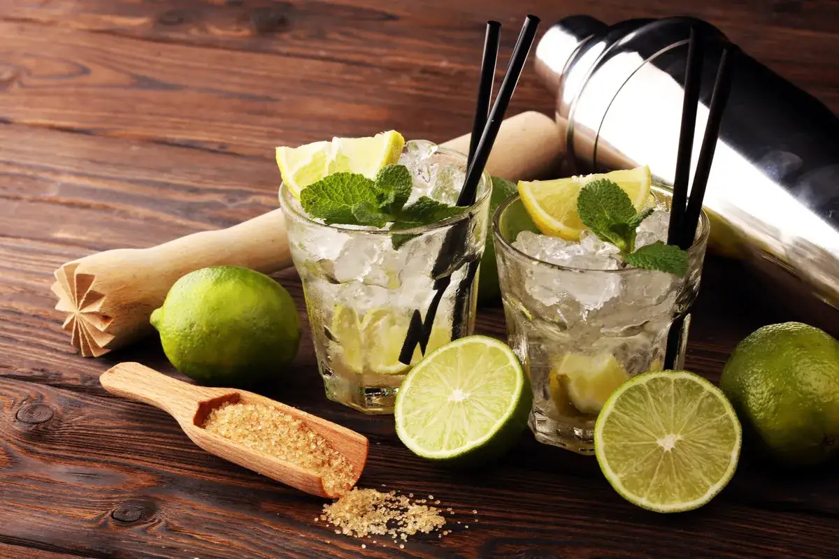 Zwei Caipirinhas mit Limetten, Minze und braunem Zucker. Was ist Cachaca? Ein brasilianischer Rum, die Basis dieses Cocktails.