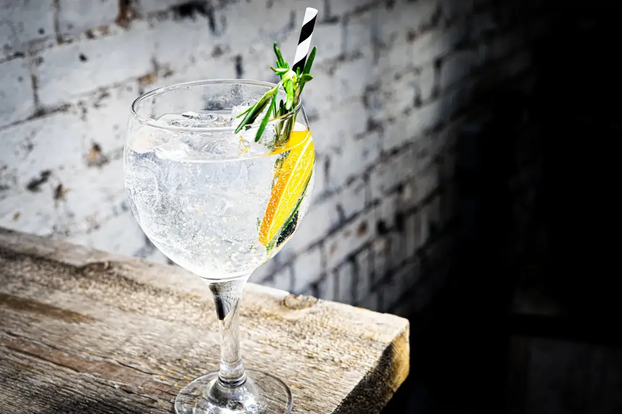 Erfrischender Gin Tonic mit Rosmarin und Zitrone, serviert auf Holztisch vor Ziegelwand.