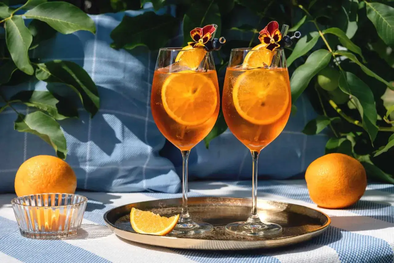 Zwei Aperol Spritz mit Orangenscheiben und essbaren Blüten. Perfekt zum Aperol mischen an einem sonnigen Tag.